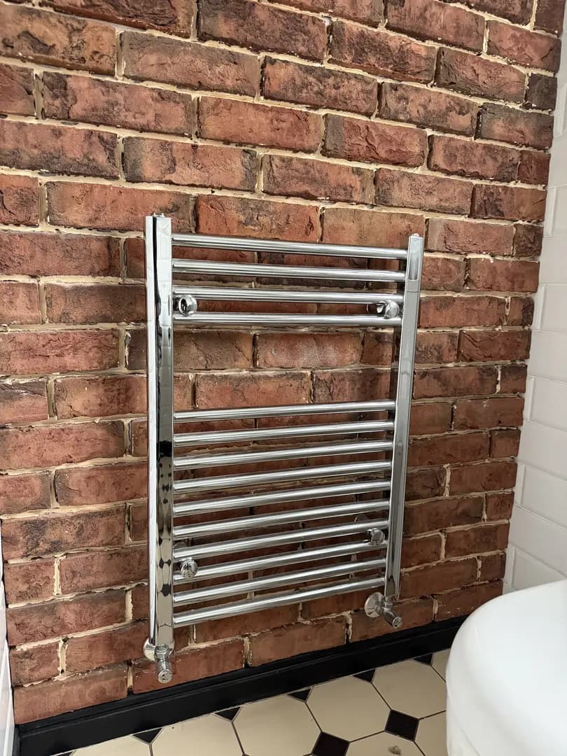 Chrome heated towel rail installation on exposed brick wall in a Bridgend bathroom